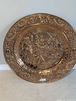 Front view of large copper dish showing intricate embossed tavern scene and decorative rim