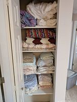Wide view of linen closet shelves filled with folded blankets, duvets, sheets, and pillowcases in various colors and patterns