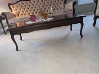 Side view of provincial style wooden coffee table with decorative curved legs and tufted furniture in background.
