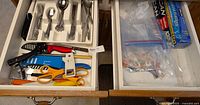 Two kitchen drawers showing various utensils and flatware. Left drawer contains scissors, can opener, bottle opener, and mostly flatware. Right drawer contains plastic wrap, aluminum foil, and plastic zipper bags.