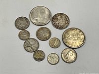 Photo showing 11 sterling silver coins arranged on a white surface for detail and size reference.