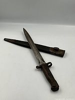 View of the 1903 Wilkerson bayonet and its metal scabbard, showing blade, wooden handle and scabbard details.