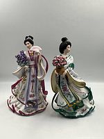 Both Danbury Mint Lena Liu porcelain figurines shown side by side on a plain background with clear details of costumes and flowers held.
