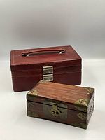 Two jewellery boxes displayed on a white background, one large red leather box and one smaller wood box with brass accents