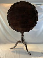 Front view of antique flip top table with round carved top in closed position, showing scalloped edges and pedestal base.