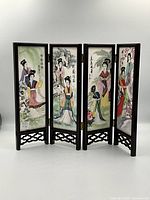 Front view showing four porcelain panels hand-painted with Asian women in traditional dress, framed in wooden frame with carved wooden base.