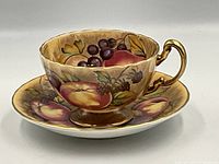 Front angled view of Aynsley Orchard cup and saucer showing detailed hand painted fruit and gold handle.
