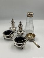 Full group of the 7 silver plated pieces including salt and pepper shakers, salt cellars with cobalt blue bowls and spoons, tea strainer, and etched glass salt shaker