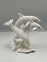 Front view of the white Lenox porcelain dolphin figurine showing three dolphins leaping over stylized waves against gray background.