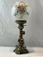 Full view of vintage brass table lamp with cherub base and floral globe shade showing overall design and height.