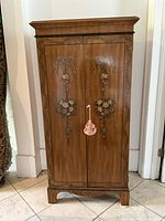 Front view of closed cabinet showing hand-painted floral doors and top molding