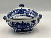 Front and side view of Flow Blue lidded jar showing deep blue scenic transferware decoration and loop handles on the sides.