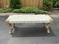 Front view of bench showing woven leather seat and driftwood frame against outdoor background