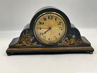 Front view of wooden mantel clock showing hand-painted Asian theme artwork in gold and colors on black background, circular gold clock face with black numbers and gold center.