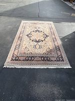 Full view of rug laid flat on asphalt, showing overall pattern and fringe.