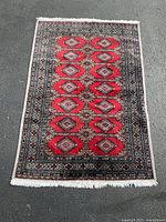 Full view of a handwoven Bokhara area rug laid flat on the ground, showing the entire red field with geometric patterns and bordered design.