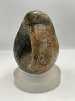 Front view of indigenous rock sculpture on frosted glass base showing natural color variations and smooth contours.