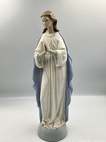 Front view of the Lladro Holy Mary figurine, showing details of face, hands in prayer, white gown with pink trim, and blue mantle.