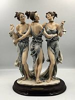 Full frontal view of porcelain statue showing three dancing women on wooden base