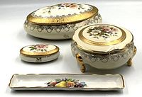 View showing all four Limoges porcelain items together: three oval lidded boxes and one rectangular tray with fruit decoration.