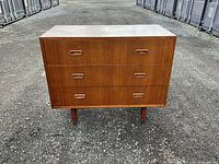 Front view of three-drawer teak dresser on pavement