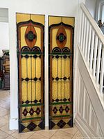 Front view of both stained glass panels leaning against a white wall near staircase