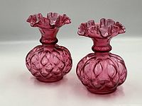 Pair of cranberry glass vases with ruffled tops shown against white background, clear view of shape and color.