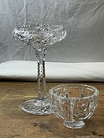 Pair of two cut crystal bowls: taller pedestal bowl and smaller round bowl side by side on wooden surface