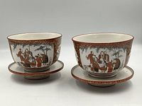 Front view of pair of bowls with saucers, showing hand painted Japanese figures and reddish-brown ornate pattern.
