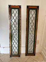 Two vertical stained glass panels leaning against a wall on a tiled floor