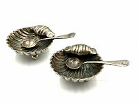 Pair of scallop-shaped salt cellars with matching spoons shown from above to display interior and spoons in situ.