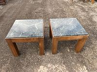 Pair of square vintage Mid Century Modern teak end tables with black marble tops on an outdoor gravel surface