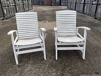 Front view of two white wooden teak deck chairs showing slatted backs and angled seats, placed outdoors on gravel.