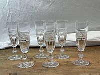 Six clear crystal champagne flutes arranged in two rows on a wooden surface with a white cloth background.