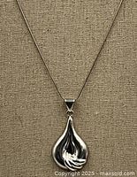 Front view of the sterling silver pendant and chain hanging against a textured surface.