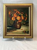 Framed acrylic painting showing a still life composition of vivid orange flowers in a brown vase on a table, signed by artist Wynne Kain.