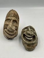 Photo shows two Inuit stone sculptures with carved expressive faces from front view on white background.