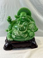 Front view of the large plastic jade-colored Laughing Buddha statue placed on a dark carved wooden stand against a neutral background.