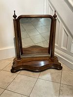 Front view of Victorian wood framed dressing mirror on shaped wooden stand with finials and visible wear.