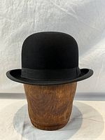 Black vintage bowler hat on wooden display stand against white backdrop