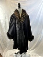 Full view of black wool cape on dress form showing large cut and fur trim along collar, front edges, and sleeve cuffs.