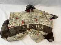Folded view showing cream background with abstract black line design, red and yellow accents, dark border with 'PRADA' logo