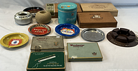 Overview of vintage tobacco tins, cigar boxes, and ashtrays arrayed on white surface with green apple for size reference.