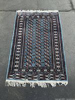 Full view of the rectangular wool area rug on pavement showing overall pattern and fringe edges.