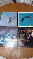 Top view of 4 vinyl record albums on a wooden surface with visible album art featuring Eagles, Steve Winwood, Asia, and La Bamba soundtrack covers.