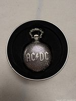 Front view of the pocket watch case showing the textured silver-tone cover with engraved ACDC logo.