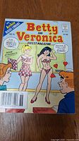 Front cover of Betty and Veronica Digest Magazine No. 76 showing Betty in a dress and Veronica in a heart patterned bikini, a humorous comic scene with two male characters watching.