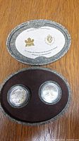 Two-coin set in protective capsules inside oval presentation case with commemorative card