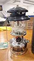 Front view of Coleman lantern showing etched glass globe, black vent cap, silver tank and limited edition badge.