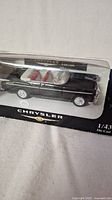 Diecast Chrysler C-300 model in original packaging showing left side profile with visible black exterior and red interior seats.